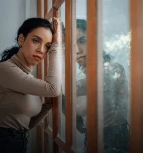 Mulher pensativa apoiada na janela
